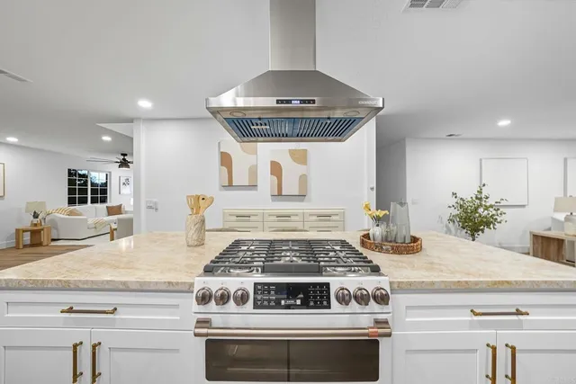 a kitchen with stainless steel appliances kitchen island granite countertop a sink a stove a refrigerator and white cabinets with wooden floor