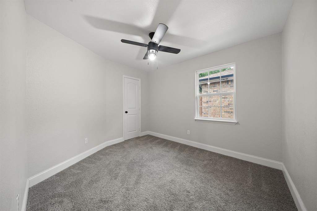 310 Valley Spring Drive Arlington, TX 76018 - Photo 18 of 24 Carpeted room with a ceiling fan, a window with white trim, a white paneled door, and neutral-toned walls