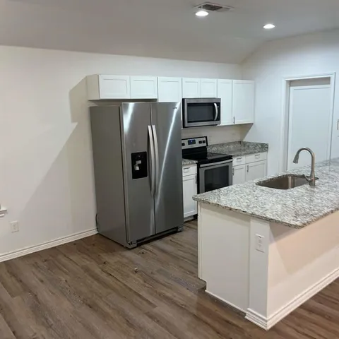 a kitchen with granite countertop a refrigerator and a stove top oven