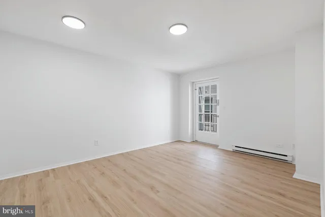 a view of an empty room with wooden floor and fan