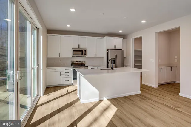 a large kitchen with stainless steel appliances granite countertop a refrigerator a sink a stove and white cabinets with wooden floor