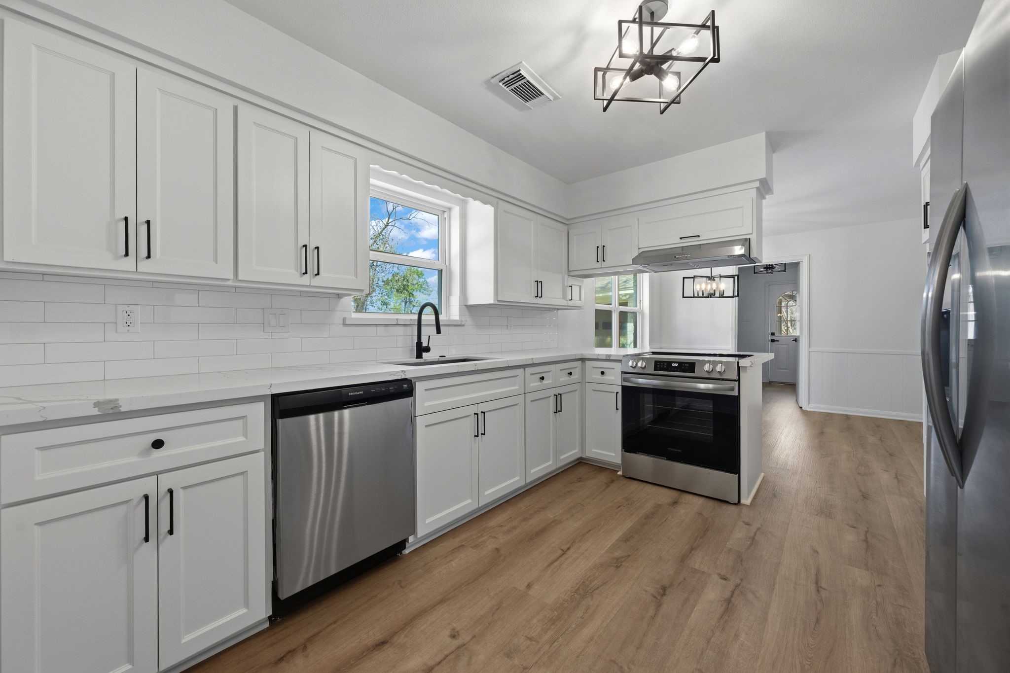 210 Ridgemont Drive Alvin, TX 77511 - Photo 6 of 27 This modern kitchen features sleek white cabinetry, stainless steel appliances, and a stylish light fixture. It has a bright, airy feel with a window over the sink and light wood flooring.