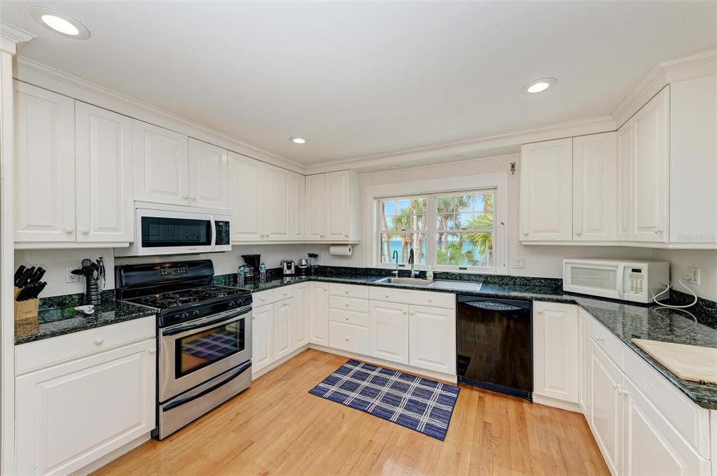 7520 Manasota Key Road Englewood, FL 34223 - Photo 71 of 96 a kitchen with granite countertop a stove top oven a sink dishwasher and a refrigerator with wooden floor