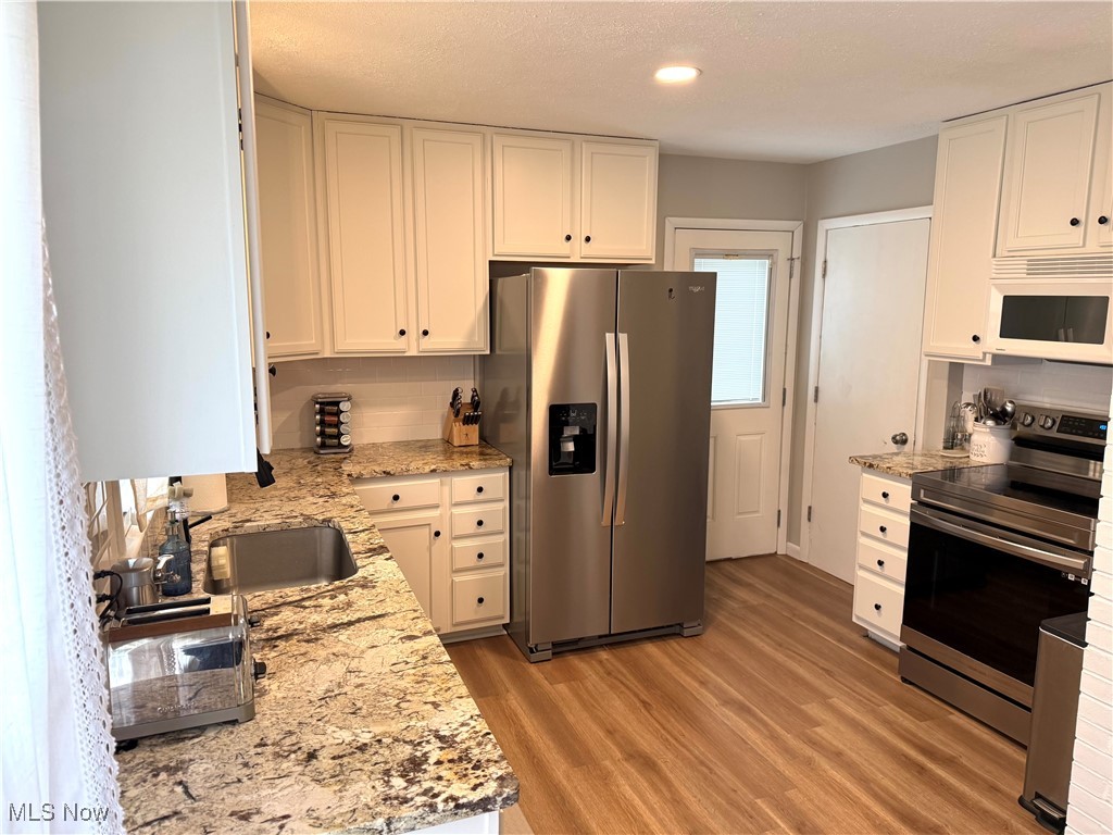 Kitchen featuring white cabinetry, appliances with stainless steel finishes, and light stone countertops