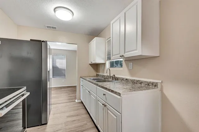 a kitchen with granite countertop a sink stainless steel appliances white cabinets and wooden floor