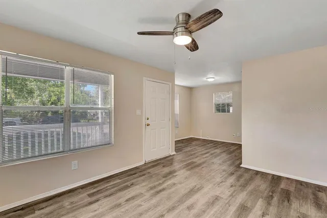an empty room with wooden floor fan and windows
