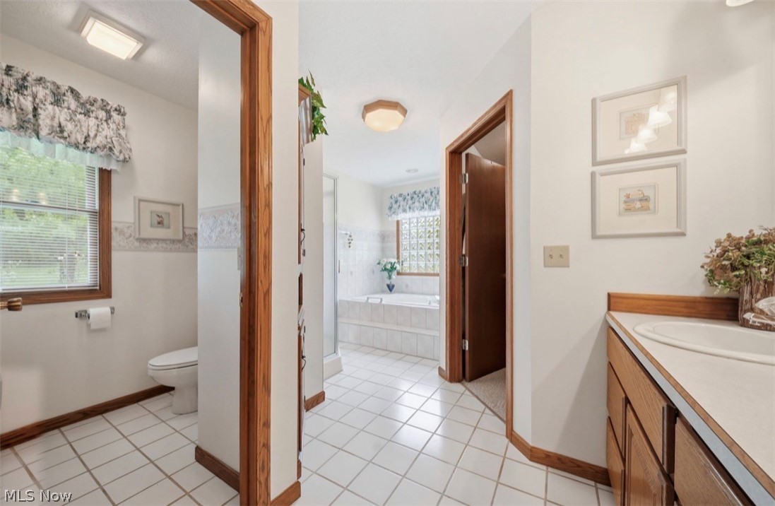3556 Lake Road Conneaut, OH 44030 - Photo 27 of 39 Bathroom featuring white square tile flooring, a built-in jetted tub, a glass-enclosed shower, a vanity with an integrated sink, and wood-trim doorways