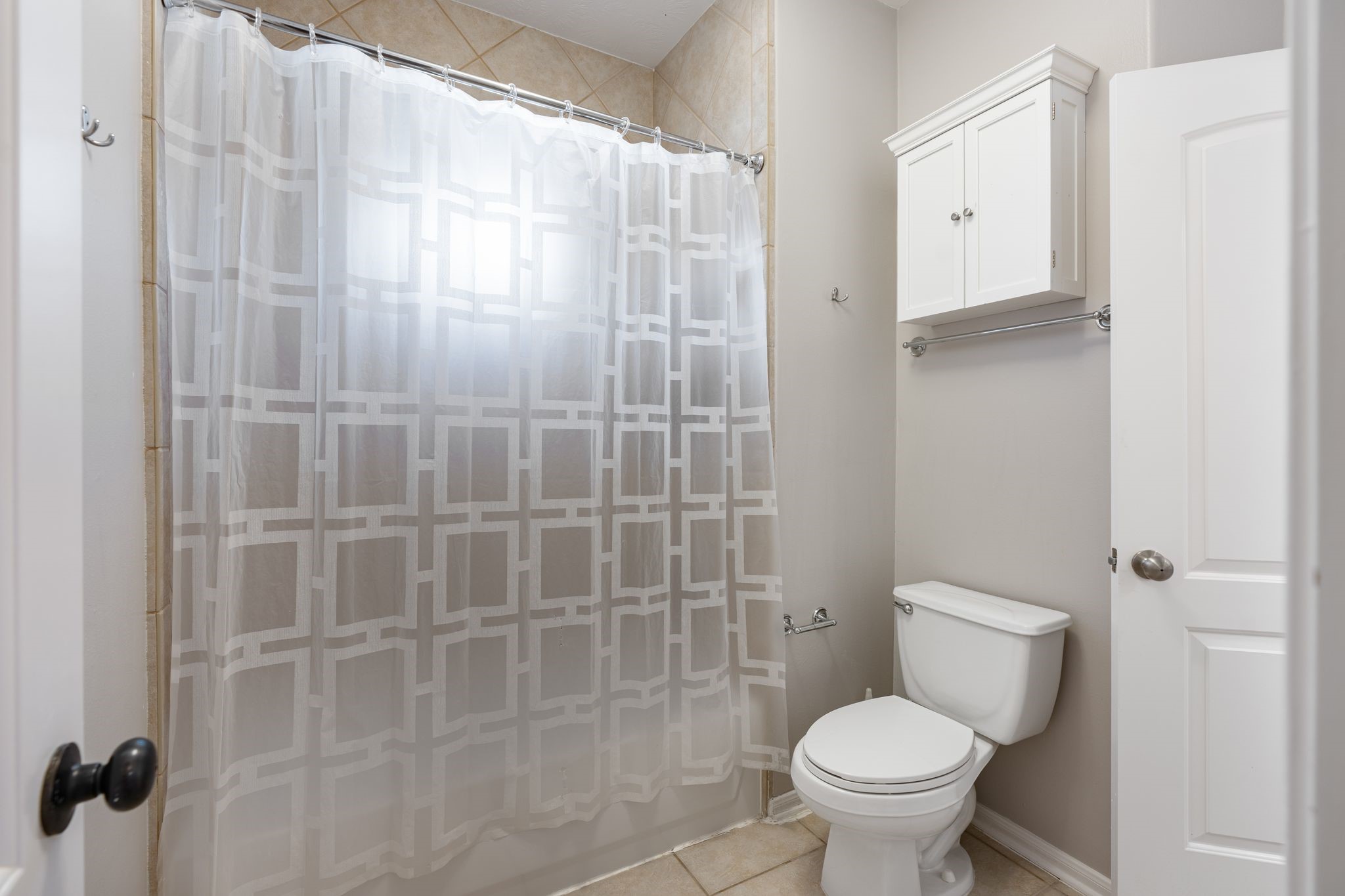 3822 Merrick Street Houston, TX 77025 - Photo 26 of 34 The wet area of this upstairs bath is shown here with the tub/shower combination, the full-height diagonal tile surround, a white upper cabinet for additional storage above the toilet, tile flooring, and chrome hardware throughout.