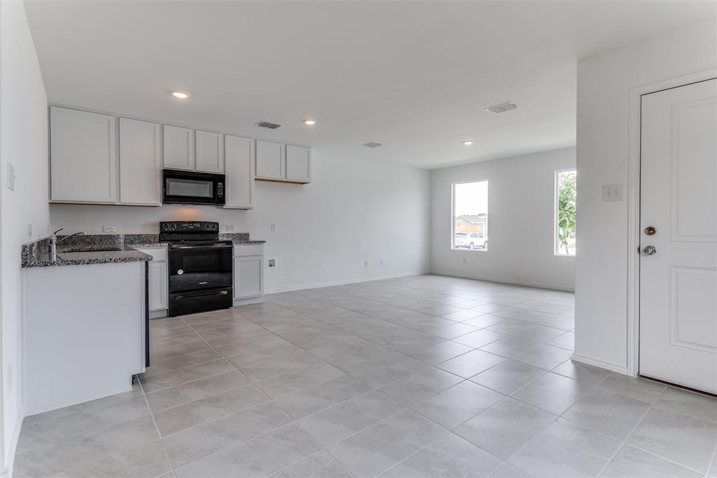 Kitchen with white cabinets, sink, light tile floors, and black appliances