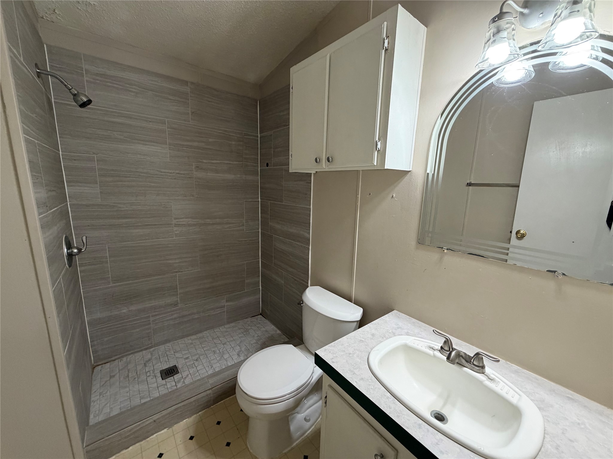 12609 Dessau Road, Unit 410 Austin, TX 78754 - Photo 11 of 11 Bathroom featuring a tiled shower with a mosaic floor, a white vanity with an integrated sink, a mirrored arch, and overhead cabinetry