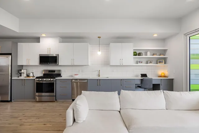 a living room with stainless steel appliances kitchen island granite countertop a sink and a stove top oven with wooden floor
