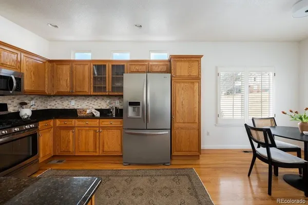 a kitchen with stainless steel appliances granite countertop a refrigerator a stove a sink a dining table and chairs with wooden floor