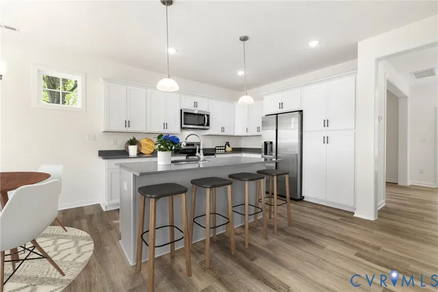 a kitchen with stainless steel appliances granite countertop a refrigerator a stove a sink a center island a dining table and chairs with wooden floor