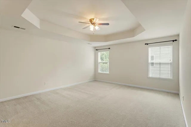 an empty room with chandelier fan and windows