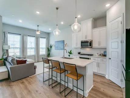 a large white kitchen with kitchen island granite countertop a stove a oven a couches and a dining table with wooden floor