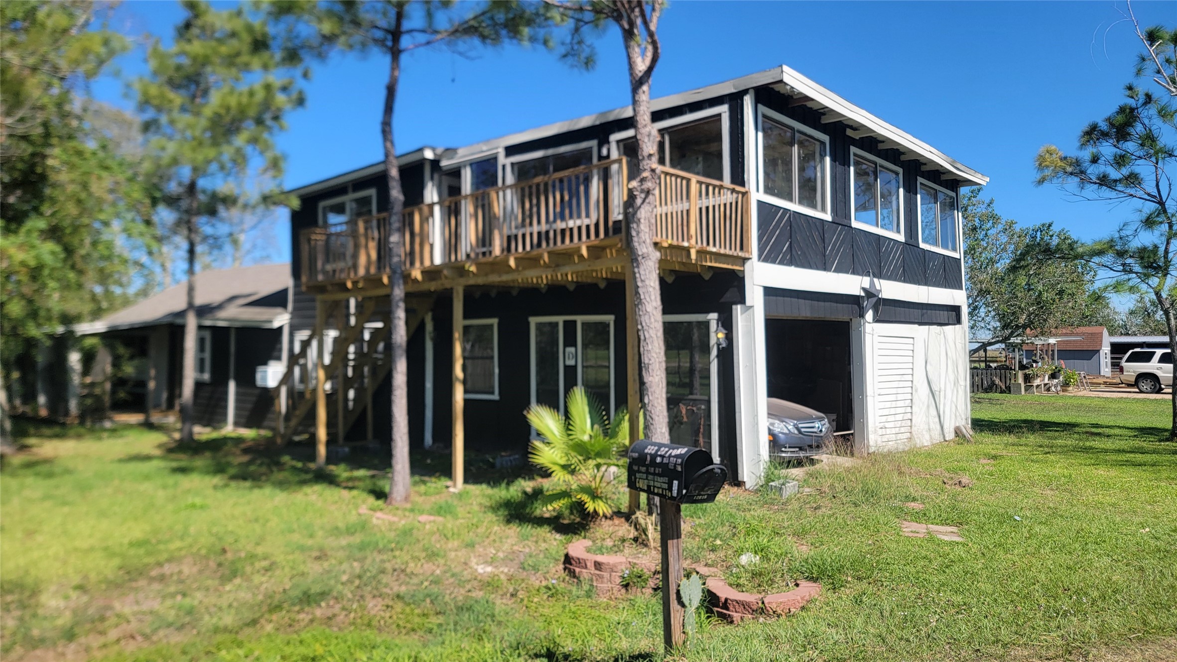 This photo features a two-story house with a wooden balcony, large windows, and a spacious garage. It's set on a grassy lot with trees, providing a serene and natural atmosphere.