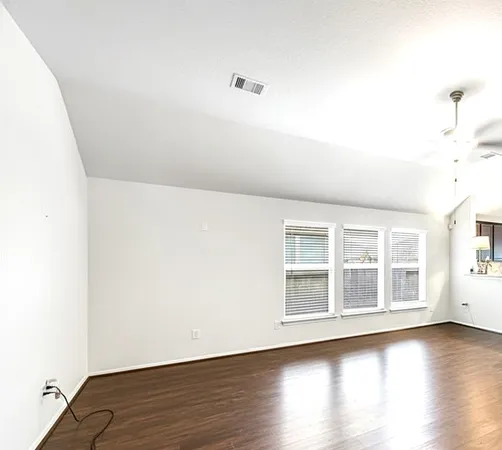 a view of an empty room with wooden floor and a window