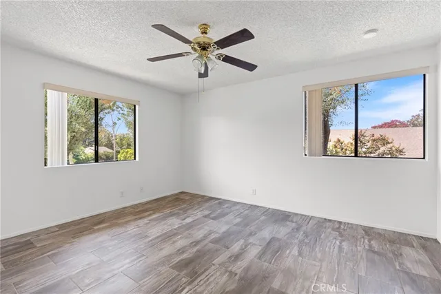 an empty room with wooden floor ceiling fan and windows