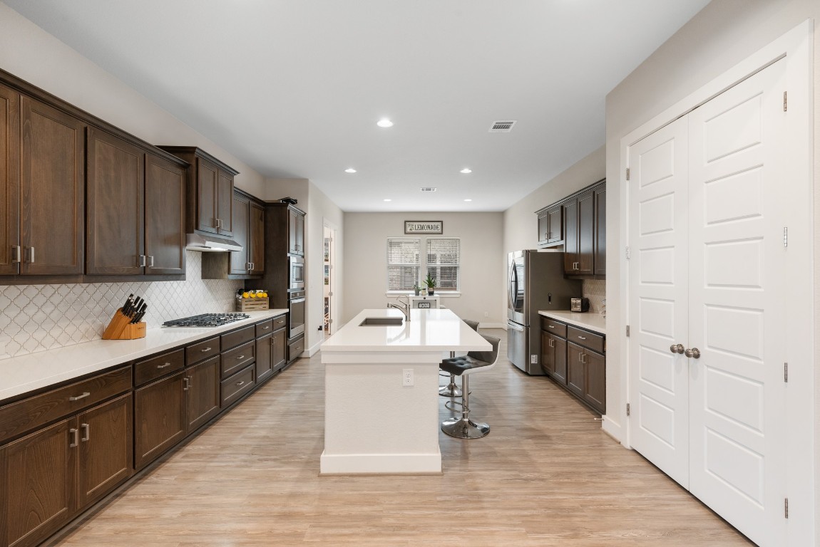216 Emerald Garden Road San Marcos, TX 78666 - Photo 14 of 38 Kitchen featuring dark brown cabinetry, a kitchen breakfast bar, tasteful backsplash, freestanding refrigerator, and light wood-style flooring