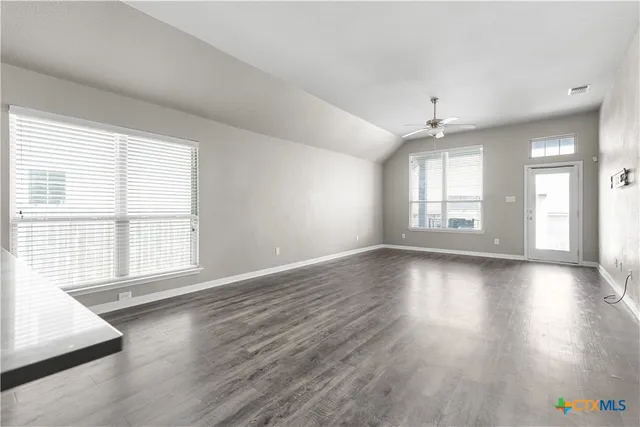 an empty room with wooden floor and windows with curtains