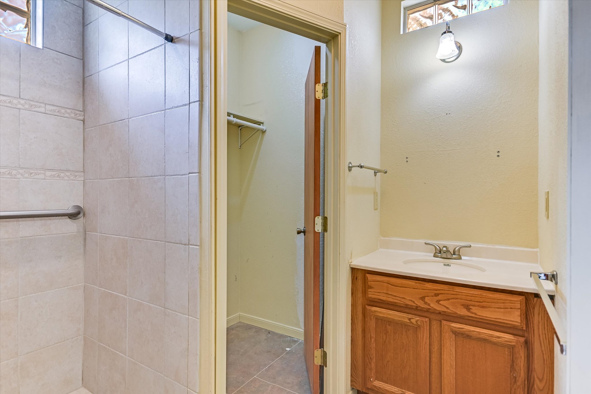 700 Cliffside Road Wimberley, TX 78676 - Photo 10 of 22 Bathroom featuring a tile-surround shower with a grab bar, wood-finish vanity with an integrated sink, wall-mounted light fixture, and a frosted glass window