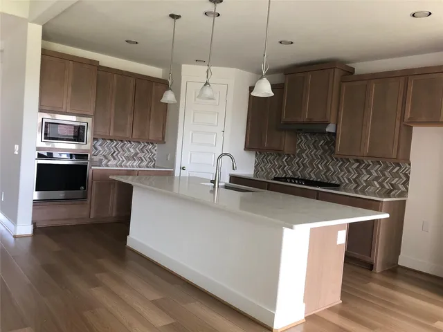 a kitchen with stainless steel appliances a sink a stove a refrigerator and island with wooden floor