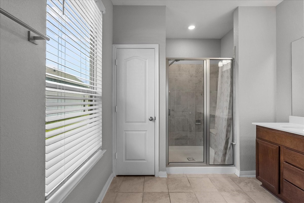 2320 Rosemary Street Rosenberg, TX 77469 - Photo 24 of 40 The bathroom features a modern walk-in shower with glass doors, a large window with blinds for natural light, tiled floors, and a wooden vanity with a sleek countertop.