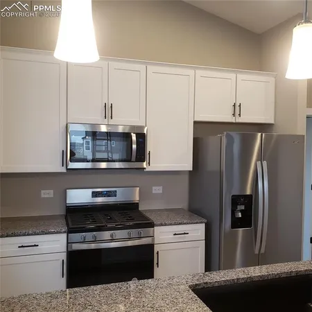 a kitchen with stainless steel appliances granite countertop a refrigerator a stove and a sink with wooden cabinets