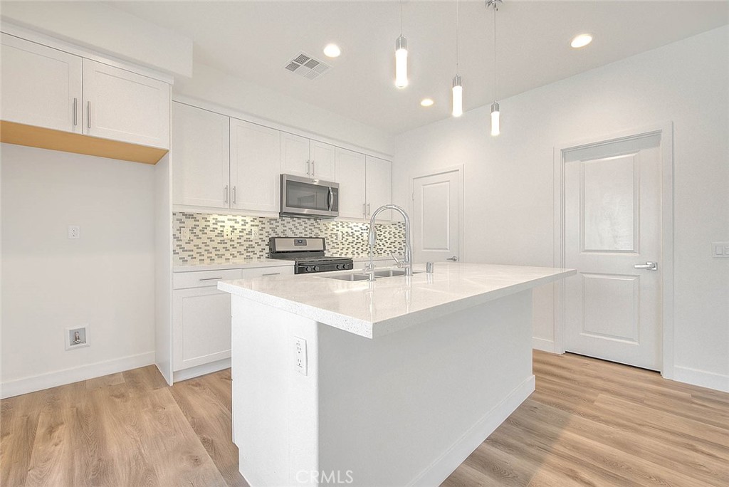 11411 VuePointe Way, Unit E El Monte, CA 91732 - Photo 13 of 38 a kitchen with kitchen island a sink stainless steel appliances and white cabinets