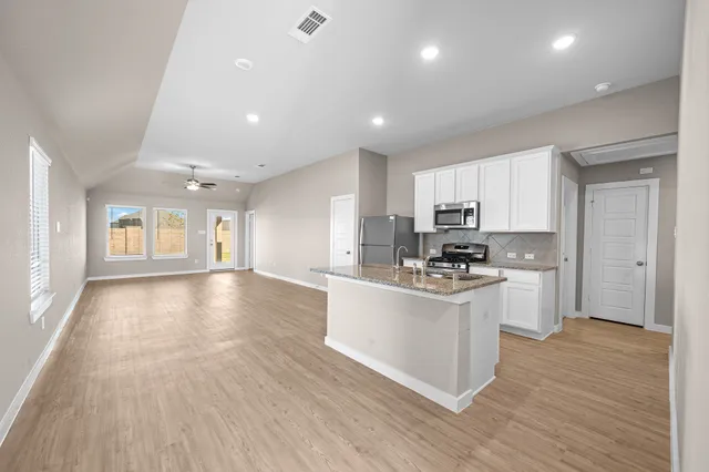 a kitchen with stainless steel appliances granite countertop a stove top oven a sink dishwasher and a refrigerator with wooden floor