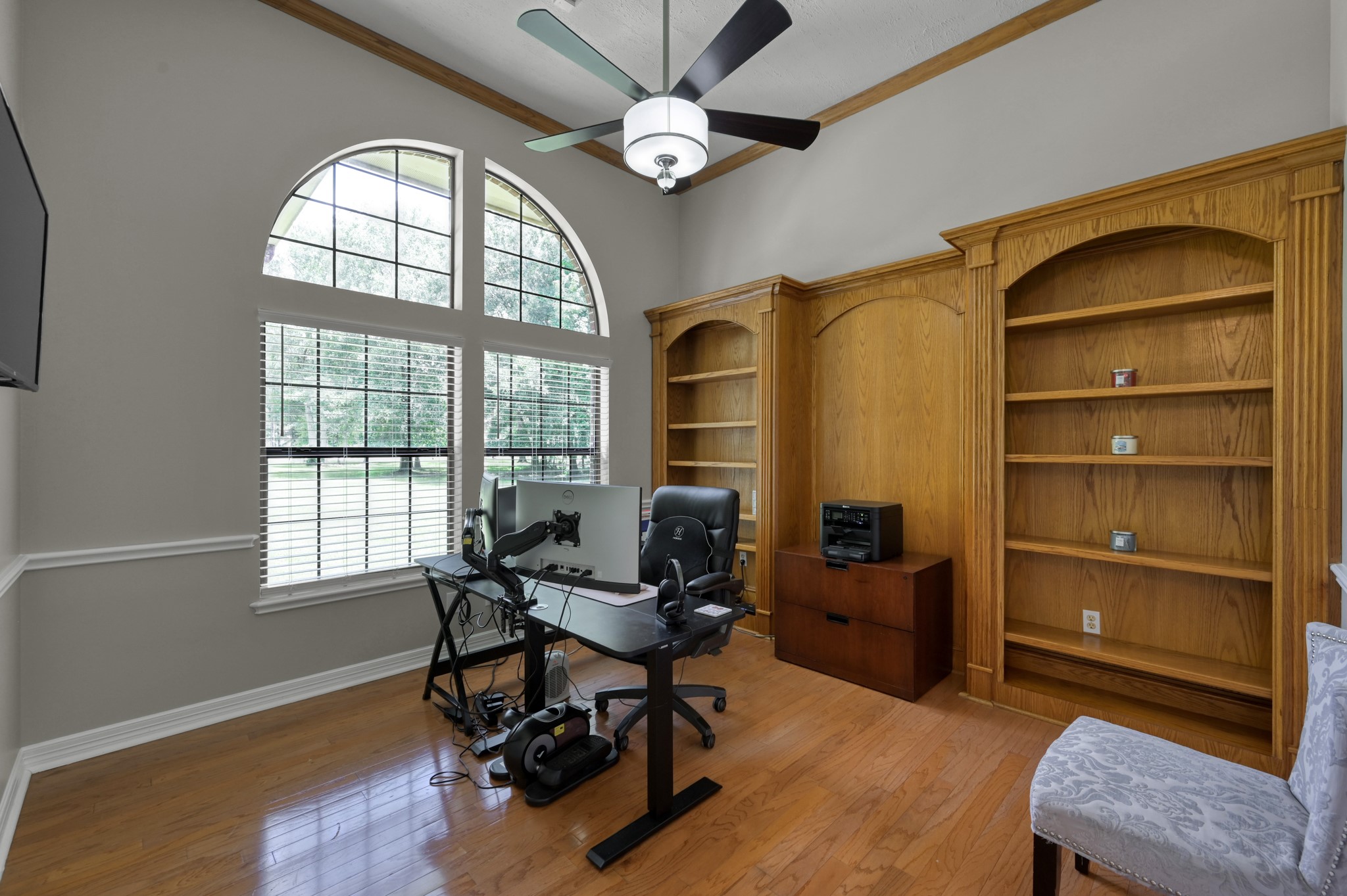 910 Commons Way Court Huffman, TX 77336 - Photo 15 of 49 This room features large arched windows providing ample natural light, elegant wooden built-in bookshelves, and a ceiling fan. It's perfect for a home office or study, with hardwood floors adding a warm touch.