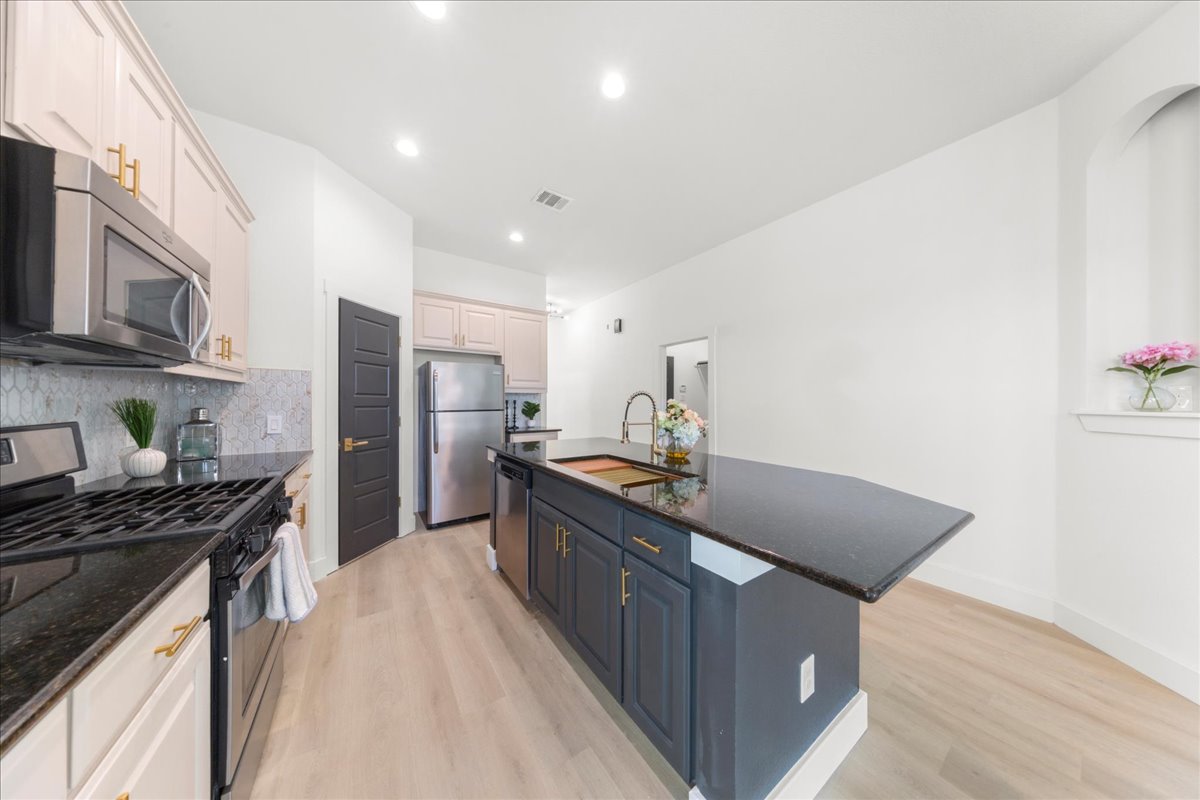 2408 Vintage Stave Road, Unit 101 Austin, TX 78748 - Photo 6 of 32 Kitchen with appliances with stainless steel finishes, dark stone counters, an island with sink, light wood-style floors, and recessed lighting