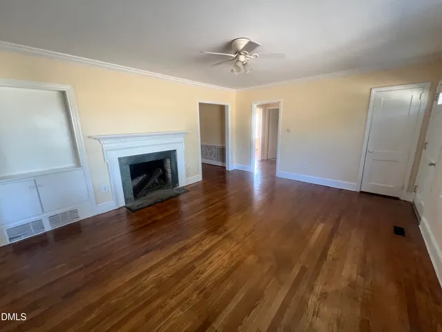 a view of an empty room with wooden floor fireplace and a window