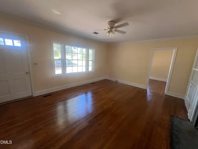 a view of an empty room with wooden floor fireplace and a window