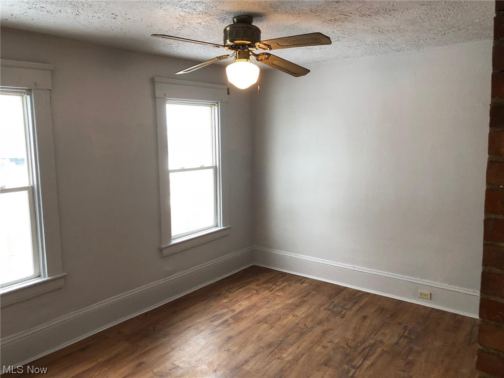 Unfurnished room featuring dark hardwood / wood-style floors, ceiling fan, a textured ceiling, and a healthy amount of sunlight