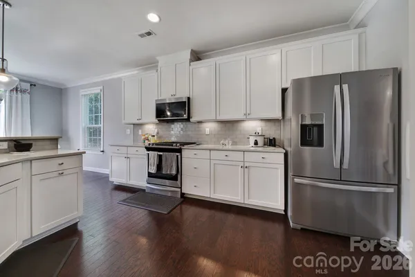 a kitchen with stainless steel appliances granite countertop a refrigerator a sink and white cabinets with wooden floor