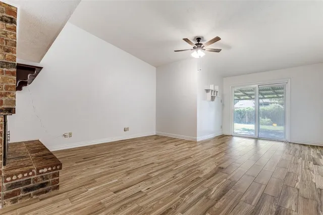 a view of an empty room with wooden floor and a ceiling fan