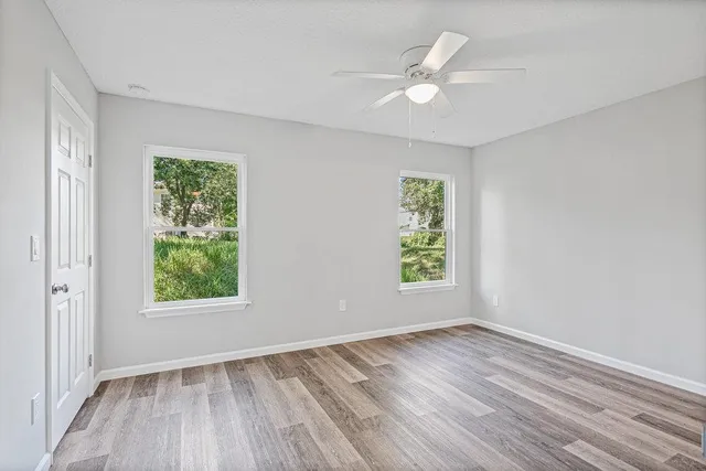 an empty room with wooden floor ceiling fan and windows