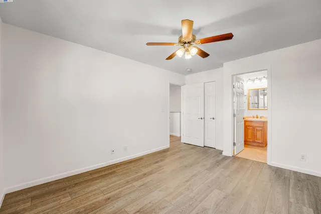 an empty room with wooden floor chandelier fan and windows
