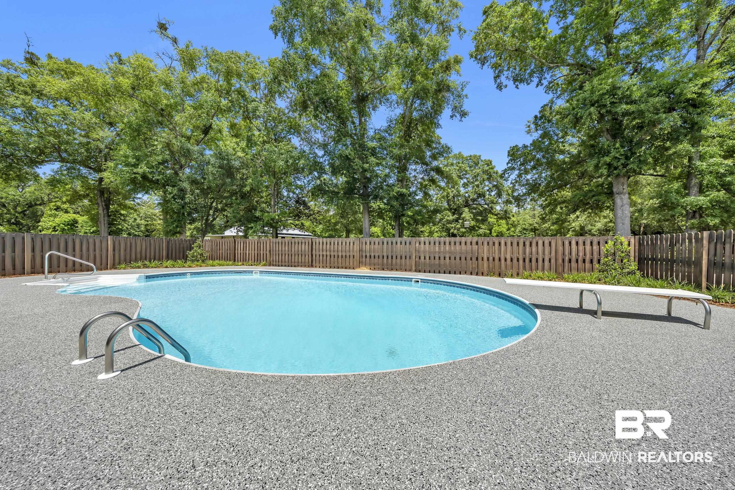 43199 Pine Grove Road Bay Minette, AL 36507 - Photo 3 of 71 Freeform swimming pool with a diving board, integrated steps, and stainless steel handrails, surrounded by a textured aggregate deck and a wood privacy fence