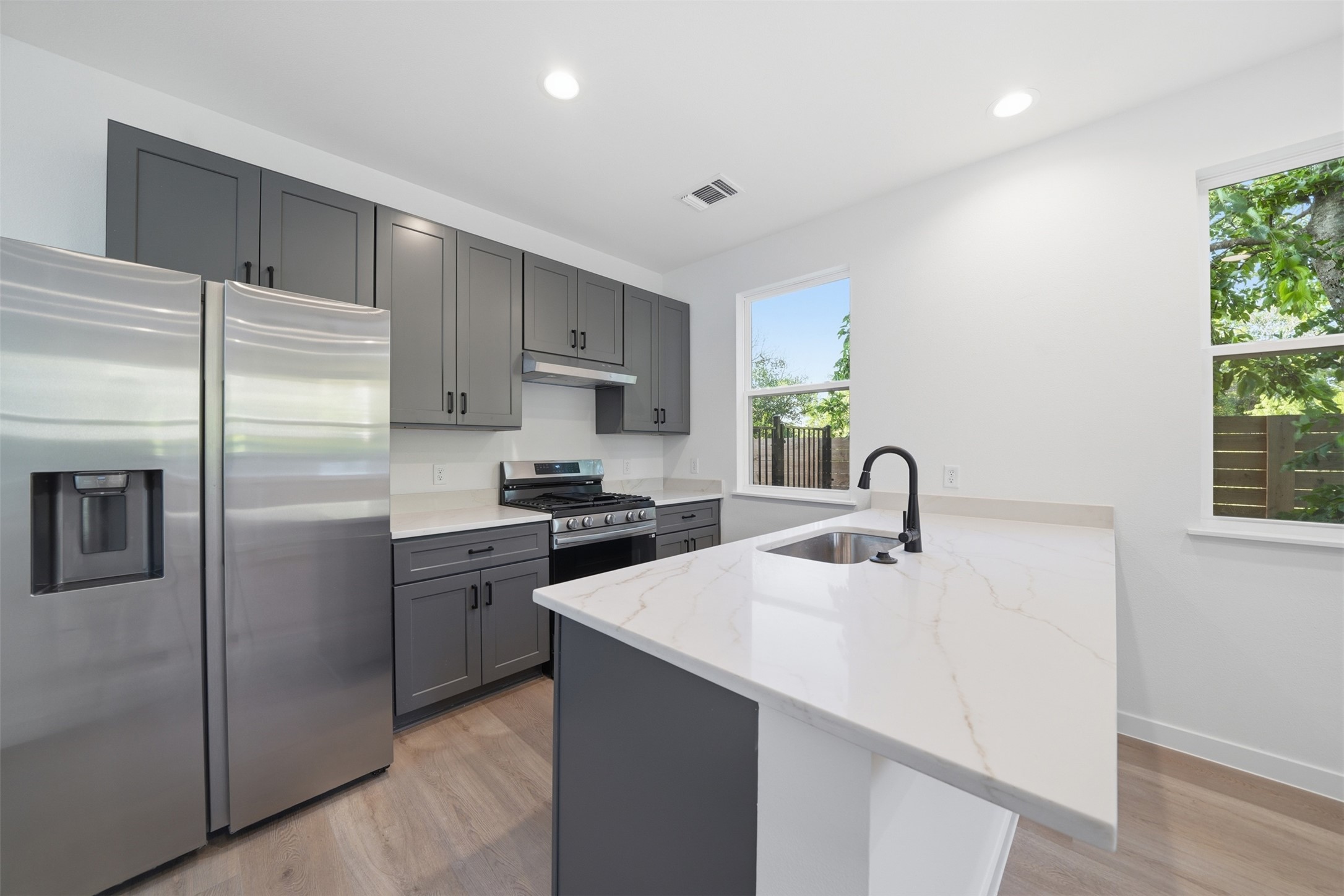 2212 Yellow Jacket Lane, Unit 2 Austin, TX 78741 - Photo 9 of 25 Kitchen featuring light wood-finish flooring, two large windows, a stainless steel side-by-side refrigerator, a stainless steel range with overhead vent, and a kitchen island with a single basin sink and matte black faucet