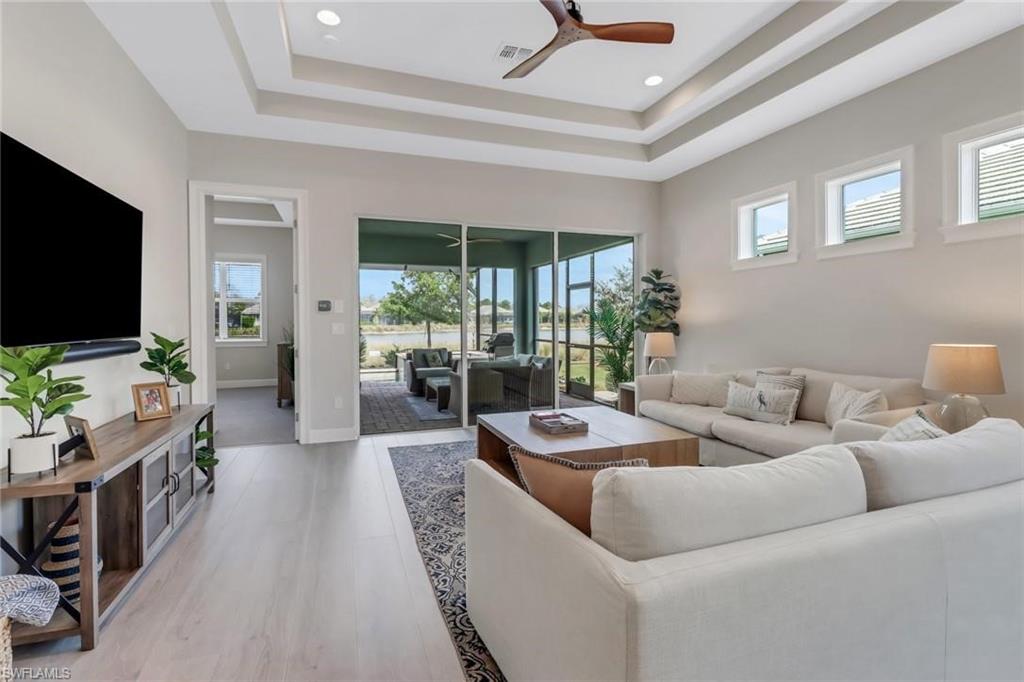 6299 Arriba Avenue Naples, FL 34113 - Photo 7 of 26 Living room with a tray ceiling, ceiling fan, and light wood-style flooring