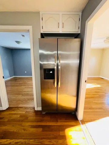 a view of a refrigerator in kitchen and an empty room with wooden floor