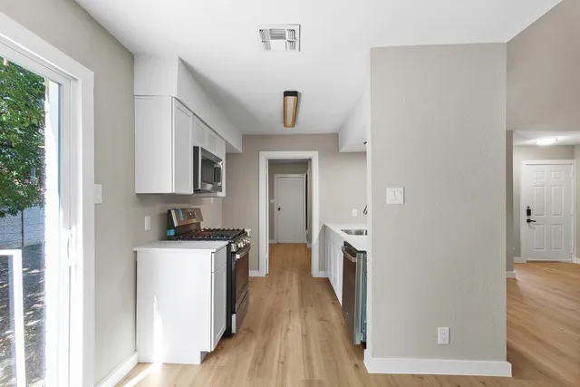 a view of a kitchen from the hallway with a white cabinets and wooden floor