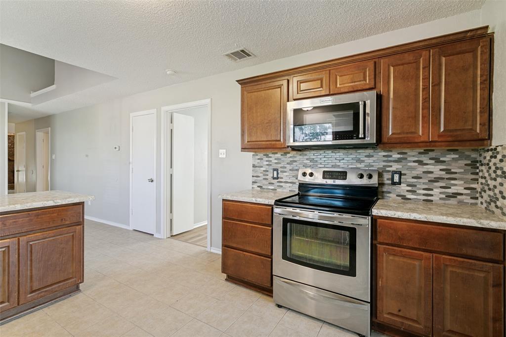 1712 East Peters Colony Road Carrollton, TX 75007 - Photo 6 of 25 Kitchen featuring wood cabinetry, light-toned countertops, a mosaic tile backsplash, stainless steel appliances, and tile flooring