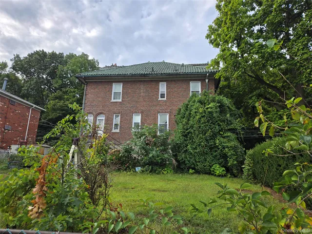 a view of a brick house next to a yard with plants and trees