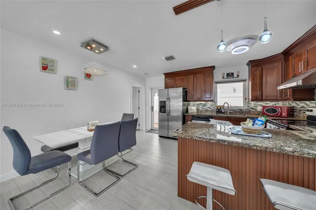 a kitchen with stainless steel appliances granite countertop a stove a sink a refrigerator dining table and chairs