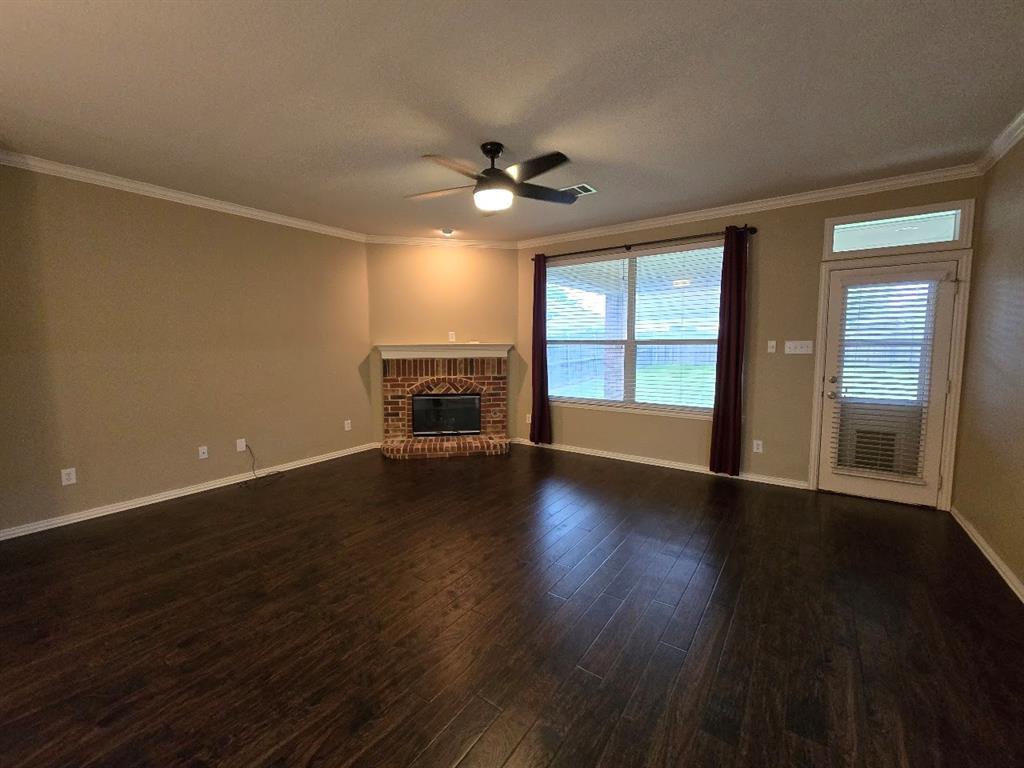 213 Willet Court Little Elm, TX 75068 - Photo 13 of 28 Unfurnished living room featuring ceiling fan, dark wood-style flooring, a brick fireplace, ornamental molding, and a textured ceiling