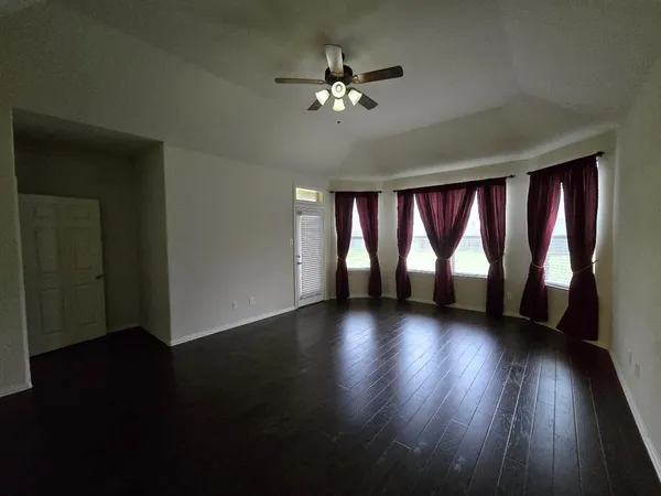 an empty room with wooden floor fan and windows