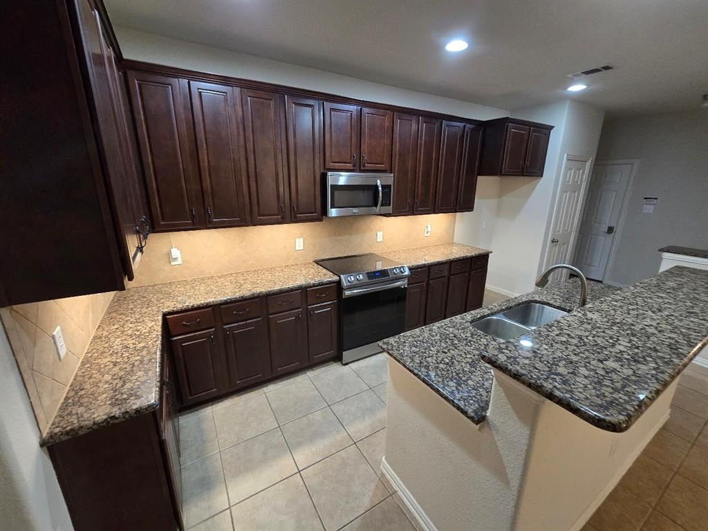 213 Willet Court Little Elm, TX 75068 - Photo 5 of 28 Kitchen with dark wood finish cabinets, stainless steel appliances, backsplash, dark stone counters, and light tile patterned floors
